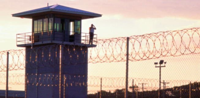 Watchtower against sunset sky, barbed wire fence