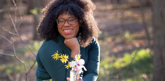 Picture of Alexis Nikole Nelson, the subject of the article, holding flowers in one hand, with hand under chin in the other 