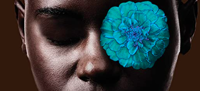 Close up of Black individual's face with blue flower over one eye