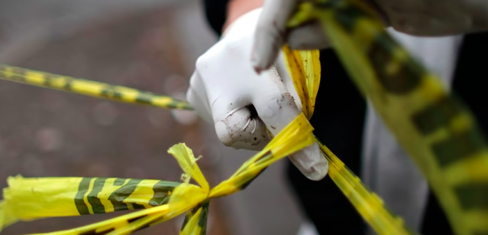 Person with white gloves handling yellow caution tape