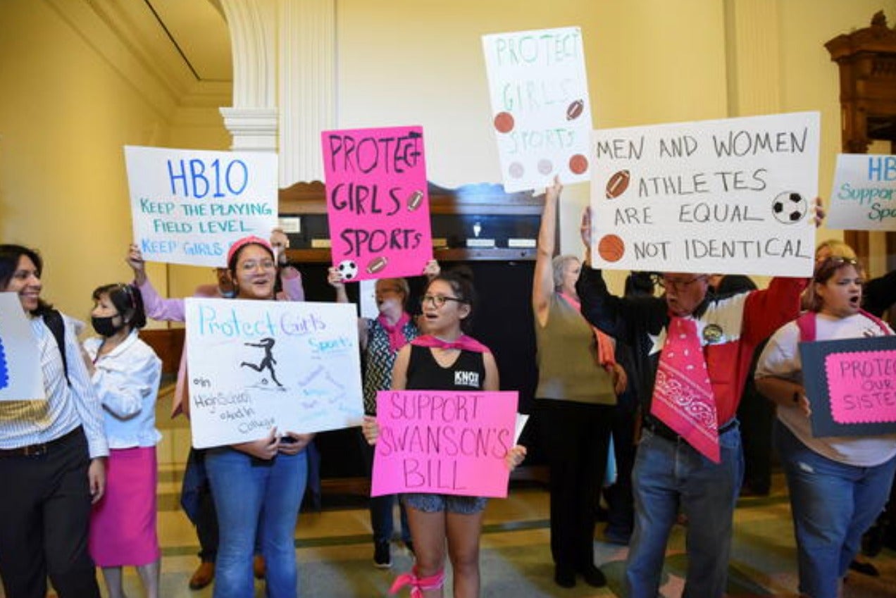 Protestors holding up signs in favor of keeping trans women out of sports