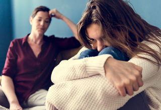 teenage girl crying into knees as mother watches